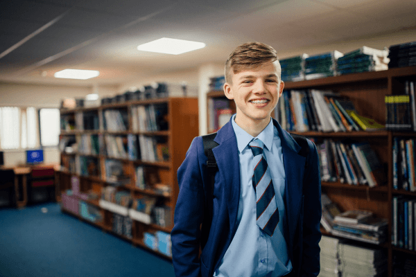 Young student in library, wearing school uniform and smiling